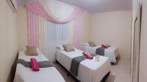 three beds in a room with pink curtains at MACEDO HOSPEDAGEM in Mateiros