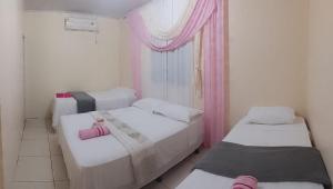 three beds in a room with pink curtains at MACEDO HOSPEDAGEM in Mateiros