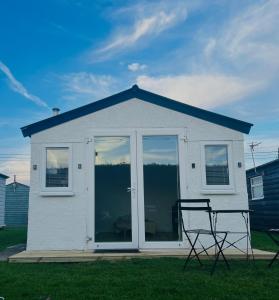 a white house with two chairs in the grass at The Cosy Summer House in Leysdown-on-Sea