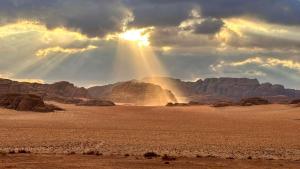 una vista del desierto con el sol brillando a través de las nubes en Magic Bedouin Star, en Wadi Rum