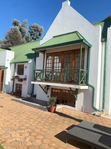 a white house with a green roof and a balcony at The Gables-Clarens in Clarens
