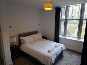a bedroom with a bed with white sheets and a window at Suffolk House Apartments HU1 in Hull