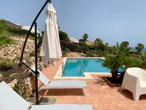 a pool with an umbrella and a chair and a table at Villa Luce in Siracusa
