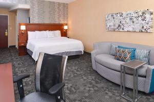 um quarto de hotel com uma cama, uma cadeira e um sofá em Courtyard Pittsburgh Monroeville em Monroeville