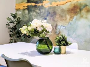 a green vase with white flowers on a table at L'Impressionniste - Spacieux - Lumineux - Central in Orléans