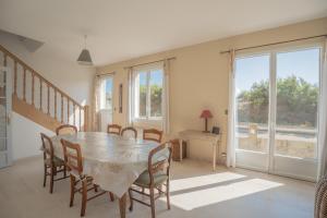 uma sala de jantar com mesa, cadeiras e janelas em Villa bord de mer pour 10 personnes em Portbail