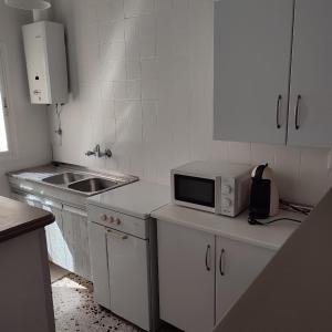 a white kitchen with a microwave and a sink at Duplex en centro de Chipiona in Chipiona