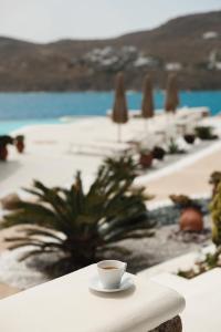 a cup of coffee sitting on a table next to a beach at Mykonos Pantheon in Kalo Livadi