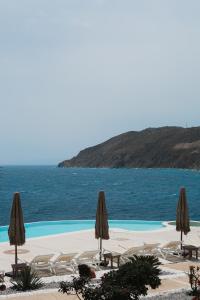 a swimming pool with chairs and umbrellas and the ocean at Mykonos Pantheon in Kalo Livadi