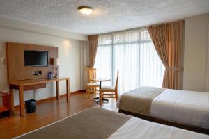 Habitación de hotel con cama, escritorio y TV. en Hotel Santa Monica en Cuenca