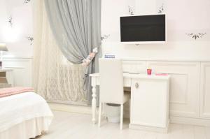 a white bedroom with a desk and a tv on the wall at Domus Rosa in Naples