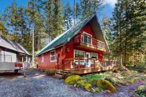 a red house with a large deck in the woods at Woodland Wanderlust in Glacier