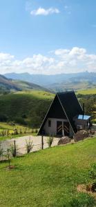 uma casa numa colina com um campo verde em Cabana Vale Encantado em São Bento do Sapucaí