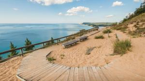 two benches sitting on a boardwalk next to the beach at Downtown Birdseye View AC 85" TV Balcony in Traverse City