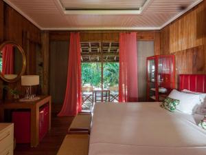 a bedroom with a bed with red curtains and a window at Hotel Vila Naià - Corumbau in Corumbau