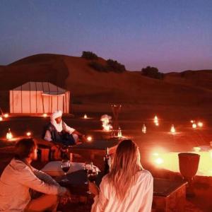 Eine Gruppe von Menschen, die an einem Tisch in der Wüste sitzen in der Unterkunft Best Luxury Camp in Merzouga