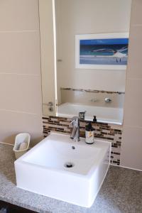 Penguin Paradise Apartment Simons Town في سيمونز تاون: حمام مع حوض أبيض ومرآة