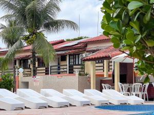 a row of white lounge chairs in front of a building at A 200m da praia de Taperapuã Axé Moi 2 suítes, churrasqueira privativa, piscina, sauna portaria 24hrs e internet privativa 300MBPS in Porto Seguro