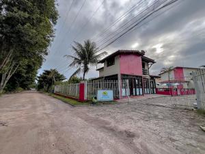 a pink building with a fence next to a dirt road at A 80m da praia de Taperapuã e da Arena Axé moi, com piscina, sauna, portaria 24hrs, acomodações com 2 ou 3 suítes, com internet privativa 300MBPS in Porto Seguro