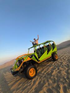 dos personas de pie en la parte superior de un jeep verde en el desierto en HOSPEDAJE WELCOME paracas, en Paracas