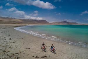 two people riding bikes on a beach near the water at HOSPEDAJE WELCOME paracas in Paracas