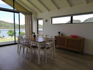 a dining room with a table and chairs and windows at Purangi Waterfront Retreat - 2 bedroom in Cooks Beach