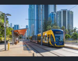 a yellow and blue train at a station with tall buildings at Oracle 2 1907 in Gold Coast