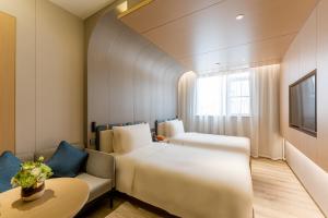 上海市にあるAtour Hotel Shanghai World Expo West Gaoke Roadのベッド2台とソファが備わるホテルルームです。