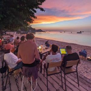 Goodtime Utopia Guesthouse في كو تاو: مجموعة من الناس يجلسون على طاولة على الشاطئ