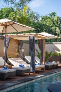 a group of beds with umbrellas next to a pool at The Compass Rose Ubud in Ubud