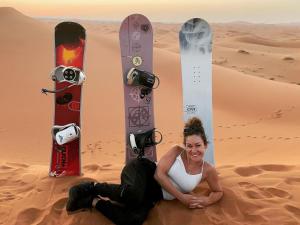 a woman sitting in the desert with two snowboards at Services Luxury Camp in Merzouga
