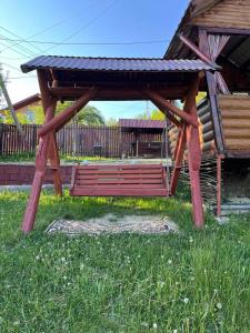 un pavillon en bois avec un banc dans l'herbe dans l'établissement Сімейний котедж КРАЄВИД, à Mykulychyn