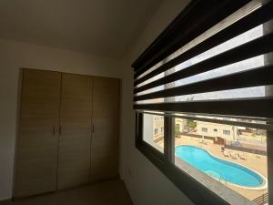 a bedroom with a window with blinds and a swimming pool at Kyklades Resort Excellence in Paralimni
