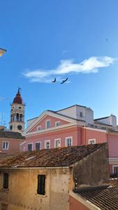 un oiseau survolant un bâtiment rose avec une tour d'horloge dans l'établissement AtticStudioTheotoki, à Corfou