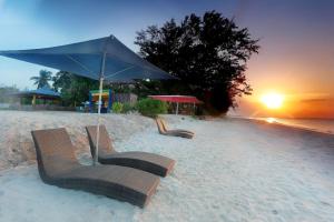 twee stoelen in het zand onder een parasol op een strand bij New Belitung Holiday Resort in Pasarbaru