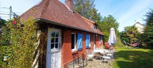 a red brick house with chairs and an umbrella at La Longère d'Auberville in Auberville