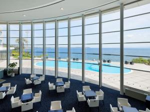 een lobby met een zwembad, stoelen en ramen bij Grand Mercure Beppu Bay Resort & Spa in Beppu