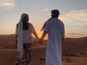 Ein Mann und eine Frau stehen in der Wüste und halten Händchen in der Unterkunft Services Luxury Camp in Merzouga