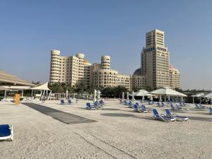 a beach with chairs and umbrellas and tall buildings at Al Hamra golf & sea resort lagoon view suite in Ras al Khaimah