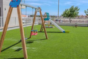 a playground with two swings on a grass field at Luxury 2 Bedroom Apartment BY KEYCITA in Los Alcázares