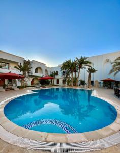 una gran piscina azul en un patio con palmeras en Palm Djerba Suites en Mezraya
