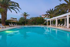 a swimming pool with chairs and palm trees at TRYP by Wyndham Corfu Dassia in Dassia