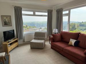 a living room with a red couch and a large window at 15 Churchfields - Bungalow with Estuary Views and Parking in Dartmouth