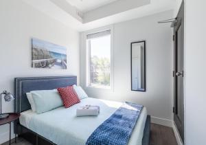 a white bedroom with a bed with red and blue pillows at Spacious 2BR Apartment - Minutes to Leslieville in Toronto