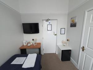 Habitación con cama, escritorio y TV. en Sussex Lodge Guest House en Slough