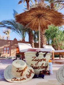 due cappelli di paglia e un ombrellone su una spiaggia di Zagora Oasis Lodge a Zagora