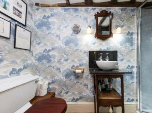 La salle de bains est pourvue de papier peint bleu et blanc et d'un lavabo. dans l'établissement Clarendon Cottage, à Enfield