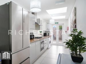  La cuisine est équipée de placards blancs et d'un réfrigérateur. dans l'établissement Large 5 Bedroom Home - Private Garden & Amenities, à Londres