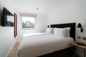- une chambre avec un grand lit blanc et une fenêtre dans l'établissement PREMIER SUITES Edinburgh Fountain Court, à Édimbourg