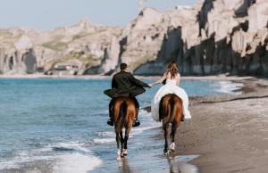 a bride and groom riding on a horse on the beach at White Note Luxury Suites in Perivolos
